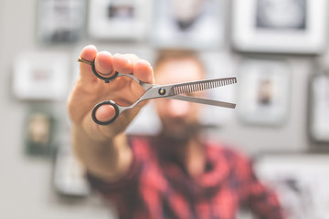 Modern man hairdresser holding sharp professional scissors at barbershop.