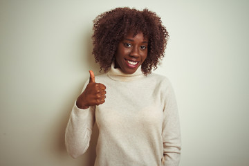 Young african afro woman wearing turtleneck sweater over isolated white background doing happy thumbs up gesture with hand. Approving expression looking at the camera with showing success.