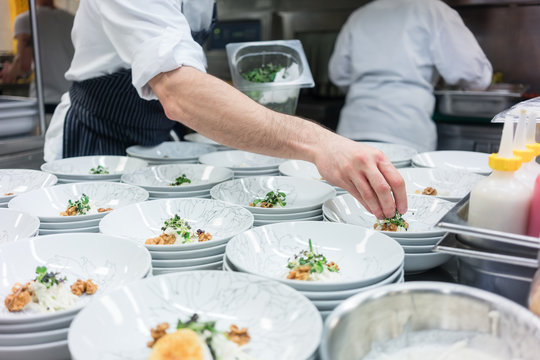 Hand of a chef styling food in multiple plates in a commercial kitchen with catering services