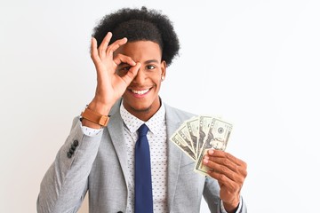 Young african american businessman holding dollars standing over isolated white background with happy face smiling doing ok sign with hand on eye looking through fingers