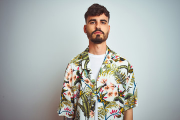 Man with tattoo on vacation wearing summer shirt standing over isolated white background with serious expression on face. Simple and natural looking at the camera.
