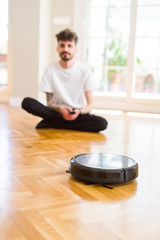 Young man using automatic vacuum cleaner to clean the floor, controling machine housework robot