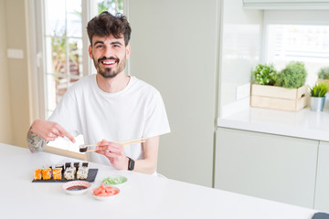 Young man eating asian sushi from home delivery very happy pointing with hand and finger