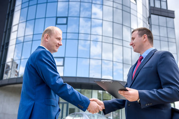 Business partners handshaking before big building outdoors