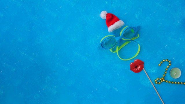 Happy New Year 2020 written by gold stones on floor tile background with lips and santa's hat on blue swimming pool background with space for your text
