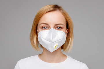 Studio portrait of young woman wearing a face mask, looking at camera, close up, isolated on gray background. Flu epidemic, dust allergy,  protection against virus. City air pollution concept 