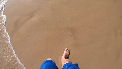 Top view from a young man walks along sandy beach and waves roll on her feet with a blue shorts