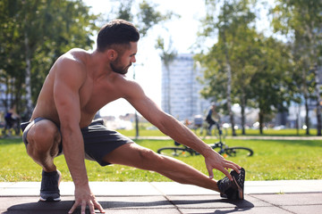 Sporty man doing workout stretching exercises for legs outdoors