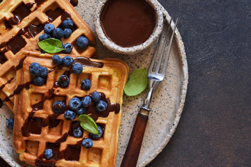 Belgian waffles for breakfast with chocolate sauce and blueberries.