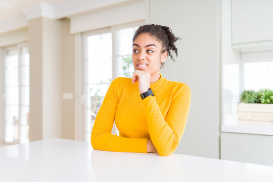 Beautiful african american woman with afro hair wearing a casual yellow sweater Thinking worried about a question, concerned and nervous with hand on chin