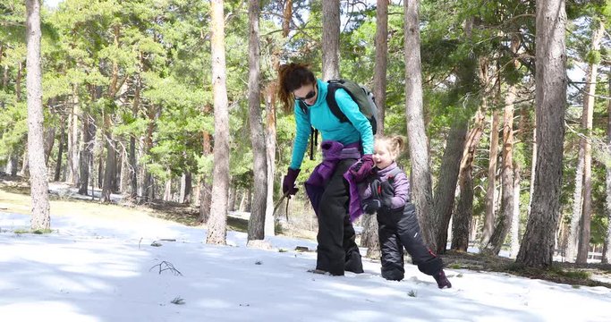 4k video. Happy family winter scene of mother and four years old child laughing, walking slowly and falling on snow in a forest of Navafria, Guadarrama, in Madrid, Spain