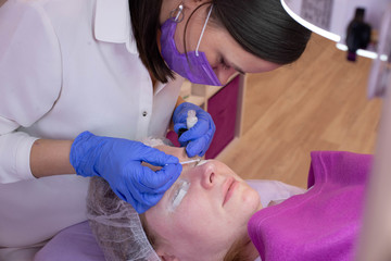 Woman on eyelash extension procedure, lamination of eyelashes in a beauty salon.