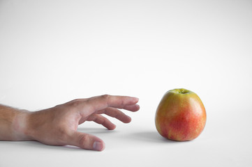 An apple stands on a white table on a white background. Hand takes apple