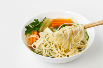 Traditional asian soup with tofu cheese, noodles, carrots and zucchini on white background, dish usually contains bouillon and vegetables, horizontal orientation