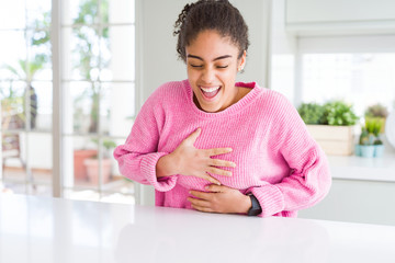 Beautiful african american woman with afro hair wearing casual pink sweater smiling and laughing hard out loud because funny crazy joke with hands on body.