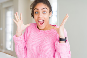 Beautiful young african american woman with afro hair celebrating crazy and amazed for success with arms raised and open eyes screaming excited. Winner concept