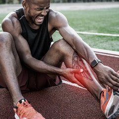 Tired sportsman suffering from knee pain at the stadium track