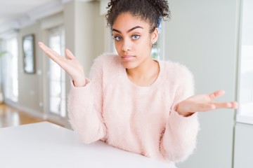 Beautiful young african american woman with afro hair clueless and confused expression with arms...