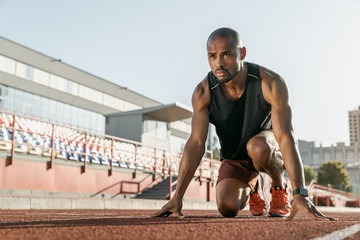 Low angle view of young man athlete in starting position for running on sports track