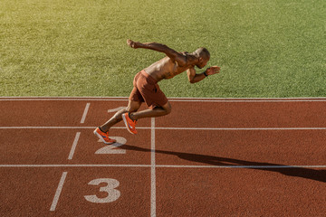 Young muscular athlete starting his running at the stadium track