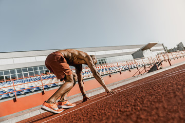 Rear view of an athlete getting ready to start his sprint on an all-weather running track
