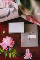 Gift bag, box and envelope with empty space on the table with peony and petals,