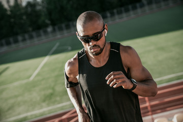 Close up of male athlete in sunglasses and earphones running up the stairs of a stadium
