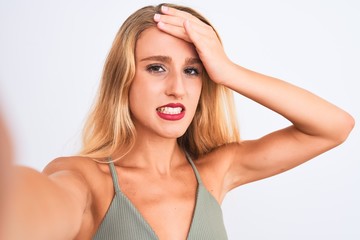 Young beautiful woman wearing t-shirt make selfie by camera over isolated white background stressed with hand on head, shocked with shame and surprise face, angry and frustrated. Fear and upset 