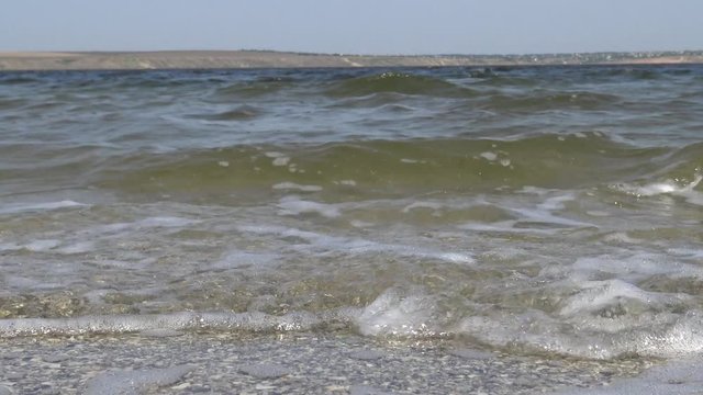 Dirty water with microalgae waves go towards the camera on the sandy spit of the Tiligul estuary, Ukraine