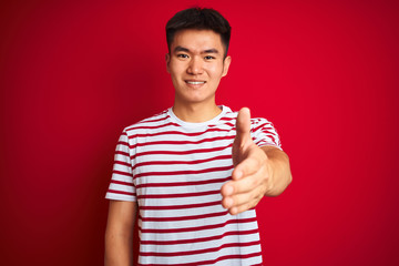 Fototapeta premium Young asian chinese man wearing striped t-shirt standing over isolated red background smiling friendly offering handshake as greeting and welcoming. Successful business.
