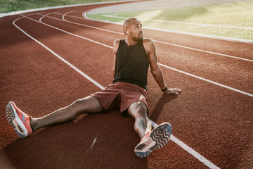Male athlete relaxing sitting on the stadium track listening to music