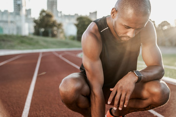 Fototapeta na wymiar Portrait of tired african male athlete finished workout and resting while sitting on a racetrack
