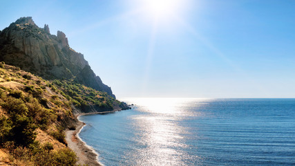 beautiful sea shore and vulcan rock mountain surrounded by ocean water panorama landscape view of Karadag mountain in Crimea with sun reflection on black sea surface natural color of nature scenery