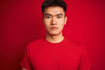 Young asian chinese man wearing  t-shirt standing over isolated red background with a confident expression on smart face thinking serious