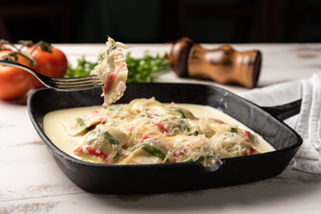 Handmade color ravioli pasta; Multi-colored ravioli pasta in a black iron pan, on wooden white table background.