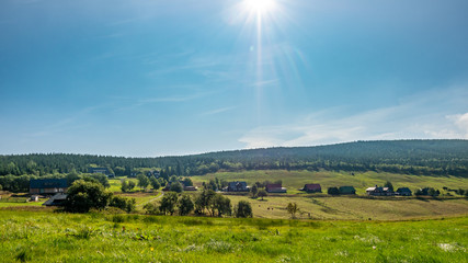 Obraz premium Green field, houses and bright sun.
