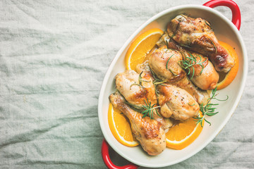 Baked chicken drumstick in a dish with orange and rosemary, top view