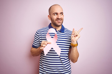 Young man holding pink brest cancer ribbon over isolated background very happy pointing with hand...