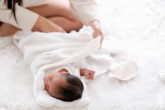 Newborn baby was swaddling with white cloth by her mother and the activity is on bed.