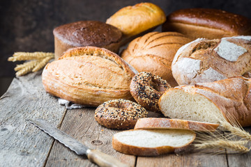 Assortment of fresh baked bread and buns on wooden table background