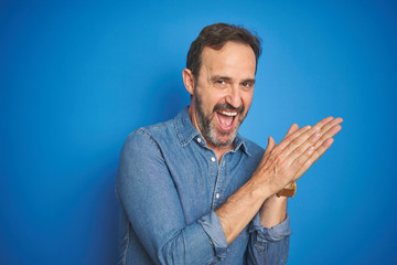 Handsome middle age senior man with grey hair over isolated blue background clapping and applauding...