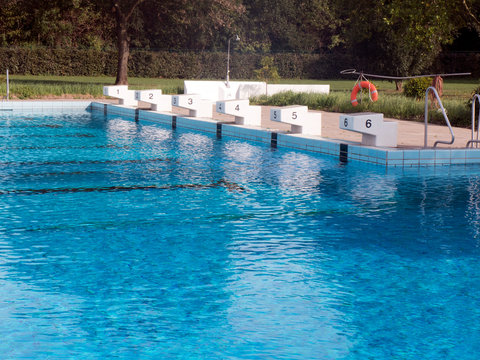 Startblöcke am Beckenrand von einem Schwimmbad. Die Blöcke tragen die Nummer eins, zwei, drei, vier, fünf und sechs. Die Startblöcke werden für Schwimmwettbewerbe genutzt .