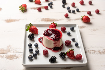 Delicious italian dessert panna cotta with berry sauce, fresh berries on white wooden background