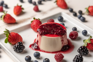 Delicious italian dessert panna cotta with berry sauce, fresh berries on white wooden background