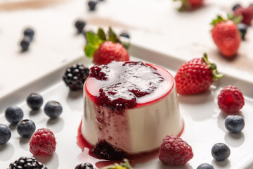 Delicious italian dessert panna cotta with berry sauce, fresh berries on white wooden background