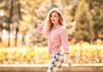 Fall outdoor. Fashionable well dressed lovable woman walking in autumn park. Beautiful blonde curly lady in trendy fashion outfit smiling enjoy sunny day. Cheerful girl relax in park, fall concept