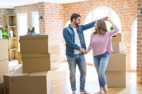 Young couple dancing celebrating moving to new apartment around cardboard boxes