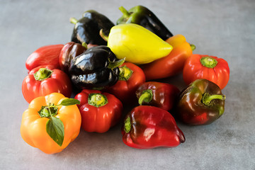 Several multi-colored paprika on a gray background.