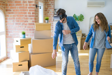 Fototapeta na wymiar Young couple moving to a new house having fun playing with virtual reality glasses around cardboard boxes