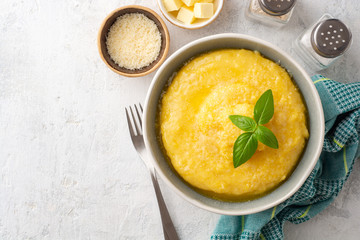 Polenta with butter and parmesan cheese in bowl on concrete background. Top view. Copy space.